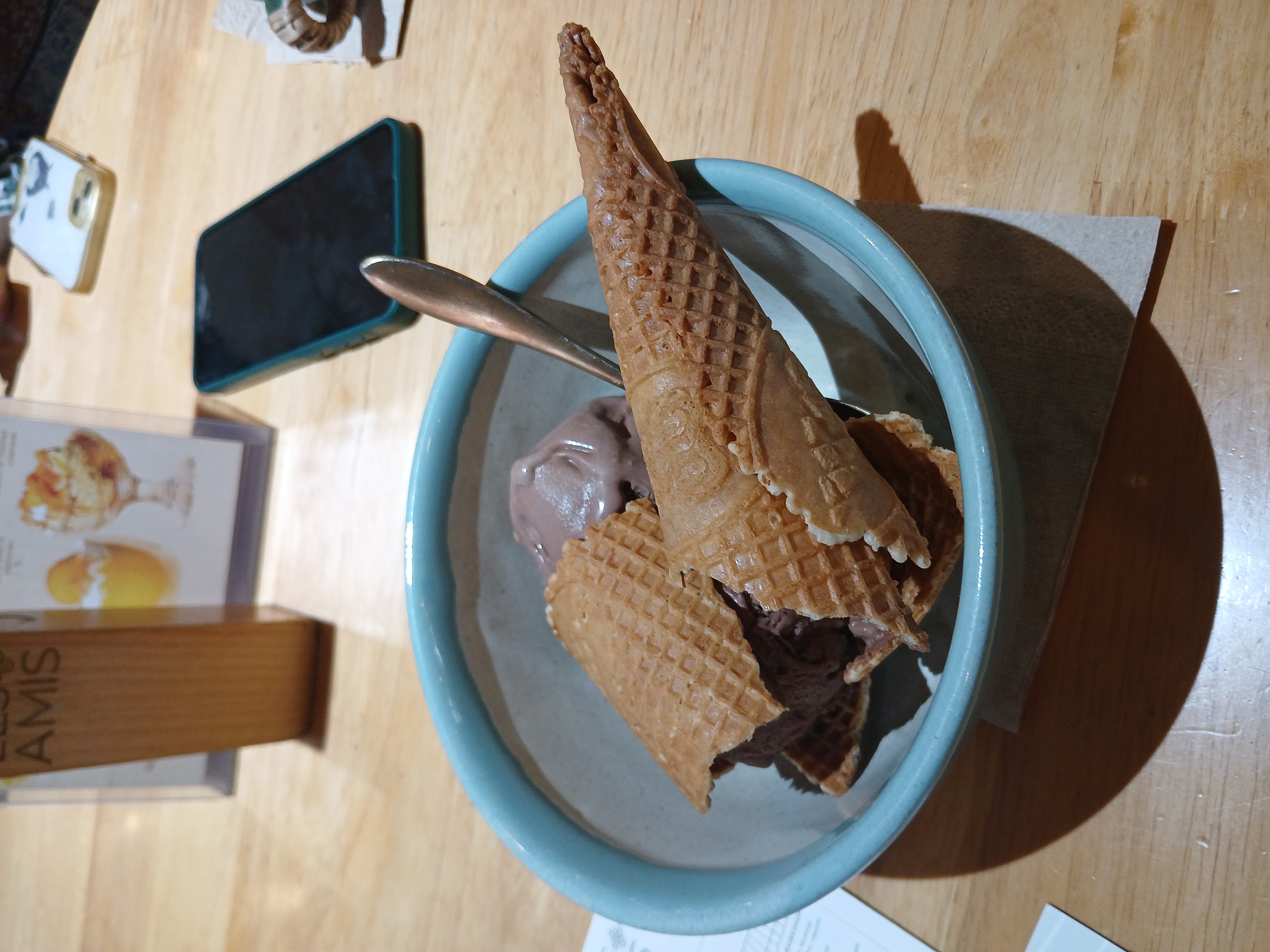image of chocolate ice-cream in a cone. the cone has been broken into half but the scoops of chocolate still remain on the top. the broken cone is in a blue ceramic bowl with a silver spoon. it looks like someone snapped the ice-cream in half.